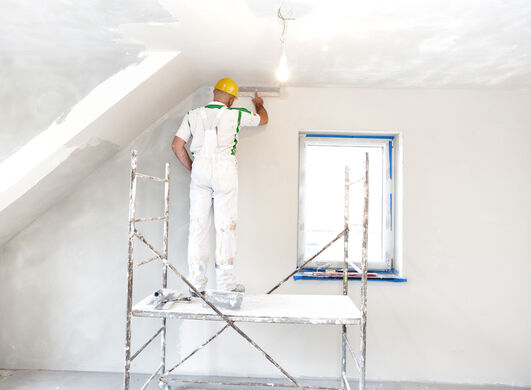 Murer står på stillads indenfor på tagetage og pudser en væg